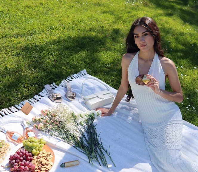 Woman sitting on picnic blanket in nature with products